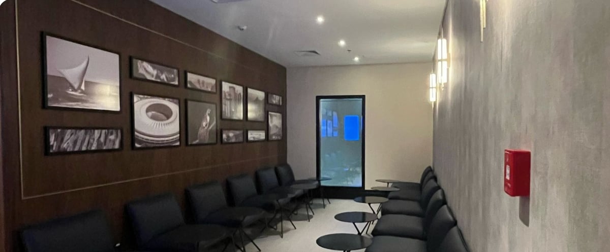 Quiet seating area at the 5th Avenue Lounge – W Premium in São Paulo GRU Airport, featuring black leather chairs arranged along the walls, small round tables, contemporary wall sconces, and framed black-and-white photography.