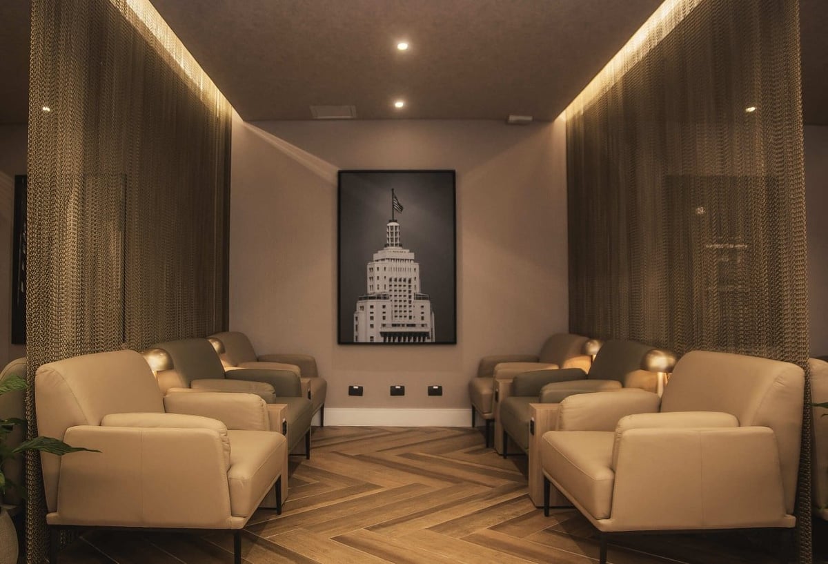 Quiet relaxation zone inside W Premium Lounge at Terminal 1 of São Paulo GRU Airport, featuring plush beige armchairs, soft lighting, privacy chain curtains, and wood-patterned flooring.