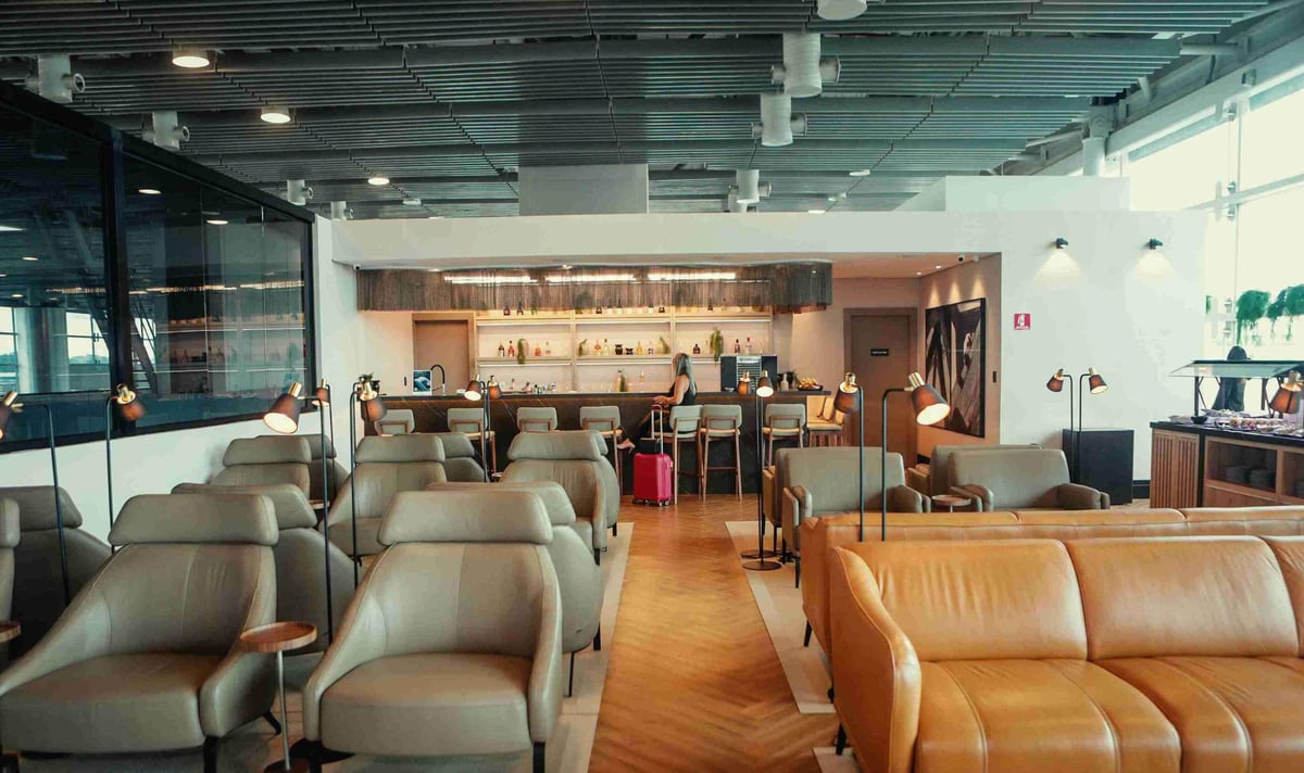 Modern seating and bar area at The Pier – W Lounge in Terminal 3 of São Paulo GRU Airport, featuring plush leather armchairs, personal reading lamps, a fully stocked bar with high stools, and buffet-style dining in a bright, contemporary setting.