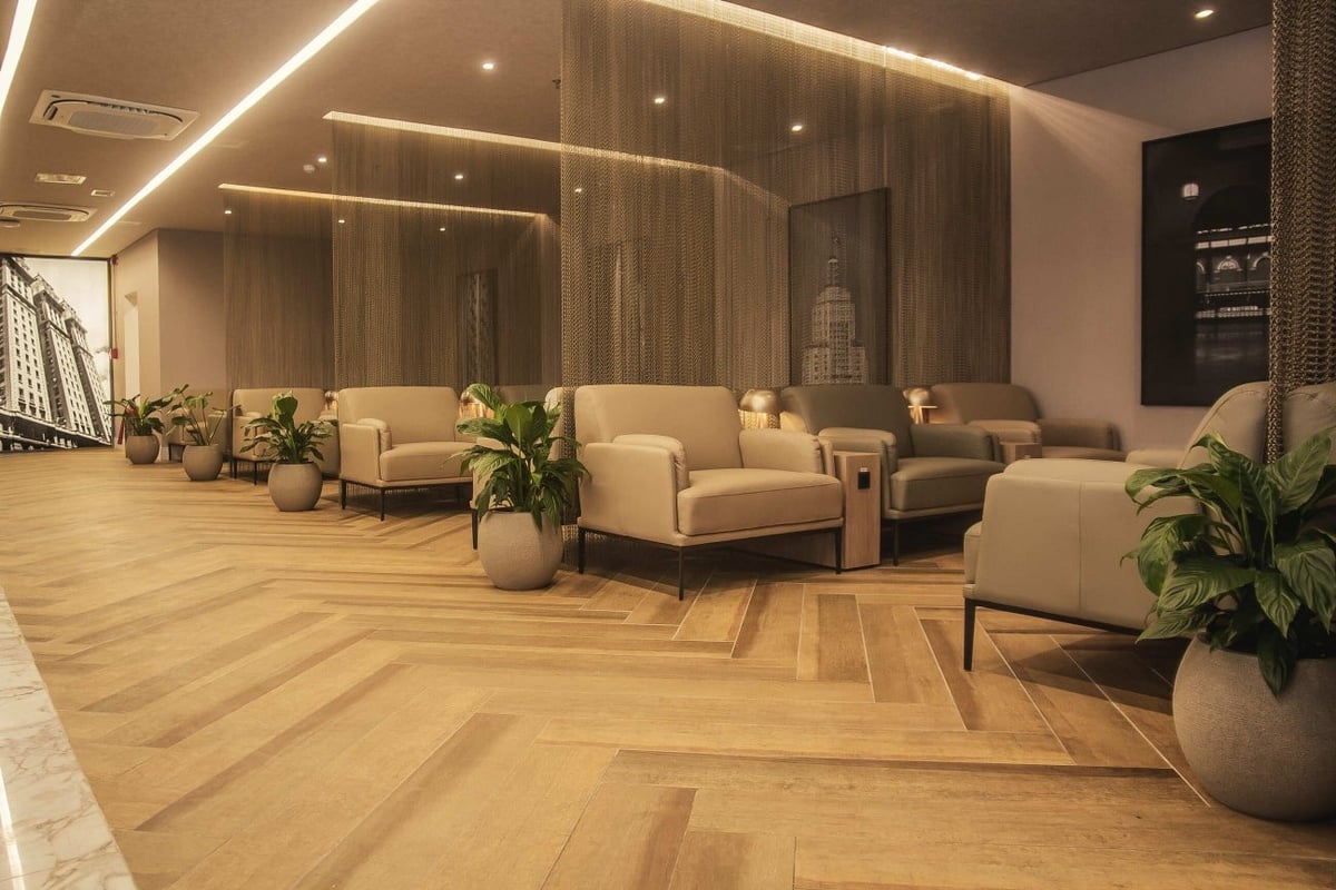 Elegant seating area at W Premium Lounge in Terminal 1 of São Paulo GRU Airport, featuring plush beige armchairs, potted greenery, warm ambient lighting, wood-look flooring, and chain mesh dividers for added privacy and comfort.