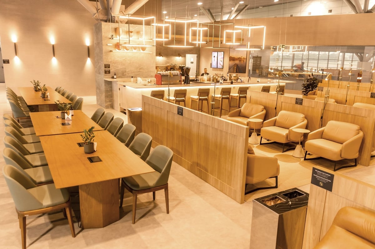 Interior of W Premium Lounge at Porto Alegre Airport showcasing modern design with leather armchairs, private seating pods, long communal tables, a sleek bar area, soft ambient lighting, and contemporary decor.