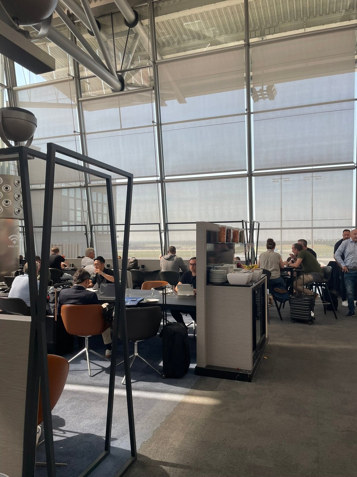 Dining or working area of the Hamburg Airport Lounge. Passengers are seated at tables, some enjoying meals, others working on laptops.