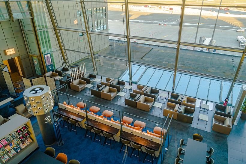This image shows an aerial view of Hamburg Airport Lounge, highlighting the spacious seating area with large floor to ceiling windows overlooking the airport tarmac.