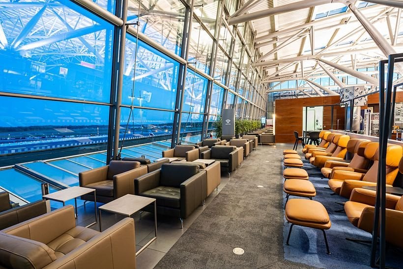 This image shows a section of Hamburg Airport Lounge, featuring a row of comfortable leather armchairs and recliners against floor to ceiling windows. The windows provide a clear view of the airport exterior, likely overlooking the tarmac and runway.