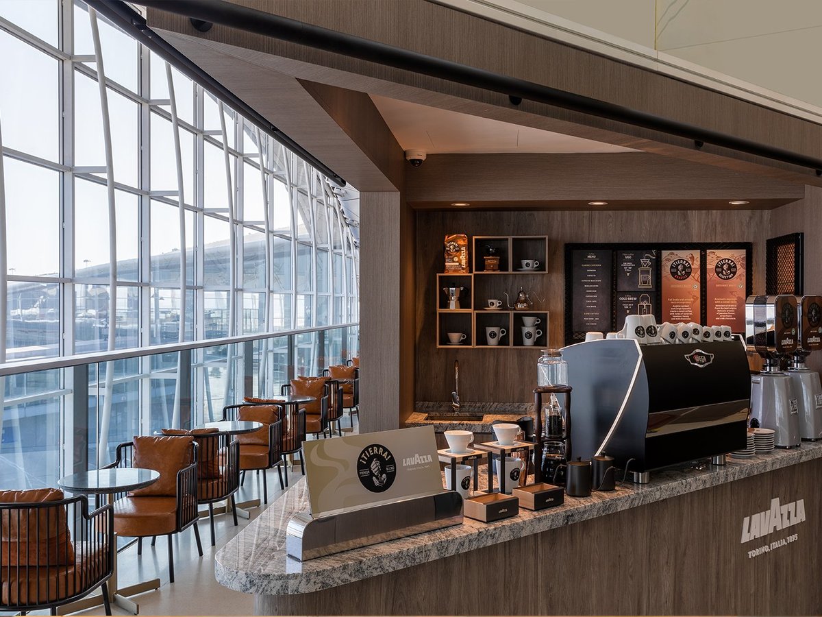 This image depicts a well-designed coffee bar area within the Hong Kong Plaza Premium Lounge Gate 60, featuring a modern espresso machine and a variety of coffee making tools and supplies branded with 'Lavazza'.
