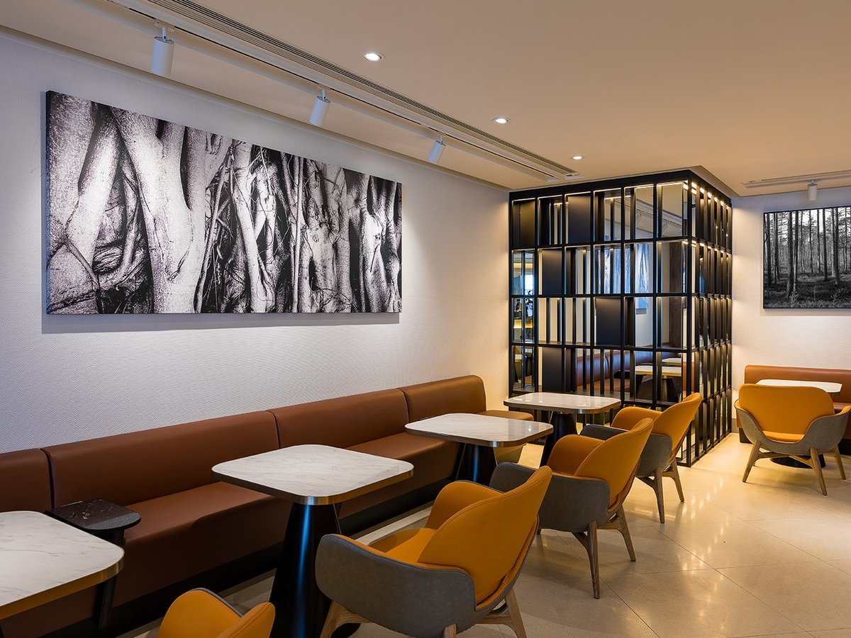 This image shows a modern and stylish seating area in the plaza premium lounge at Hong Kong Airport. The space features a row of marble tabletops, paired with comfortable chairs upholstered in a combination of warm brown and grey tones.