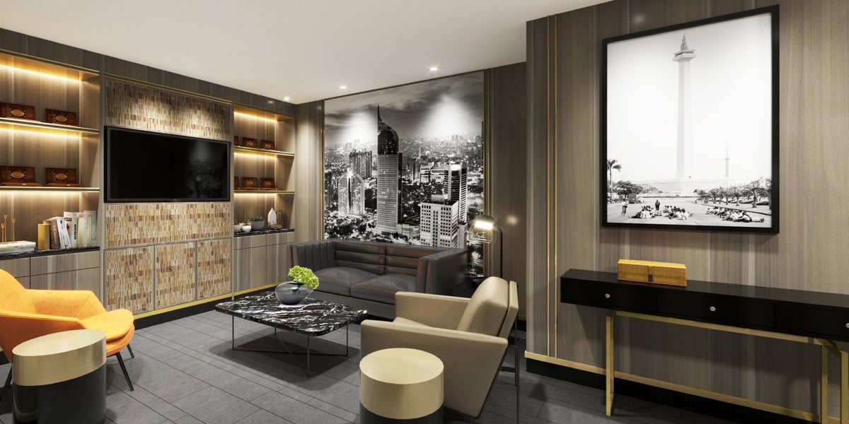 Lounge area at the Jakarta Saphire Plaza Premium Lounge. The room features a large TV mounted on a wall with decorative paneling. There are built in shelves with books, decorative items and accent lighting. A black and white city mural is on the wall