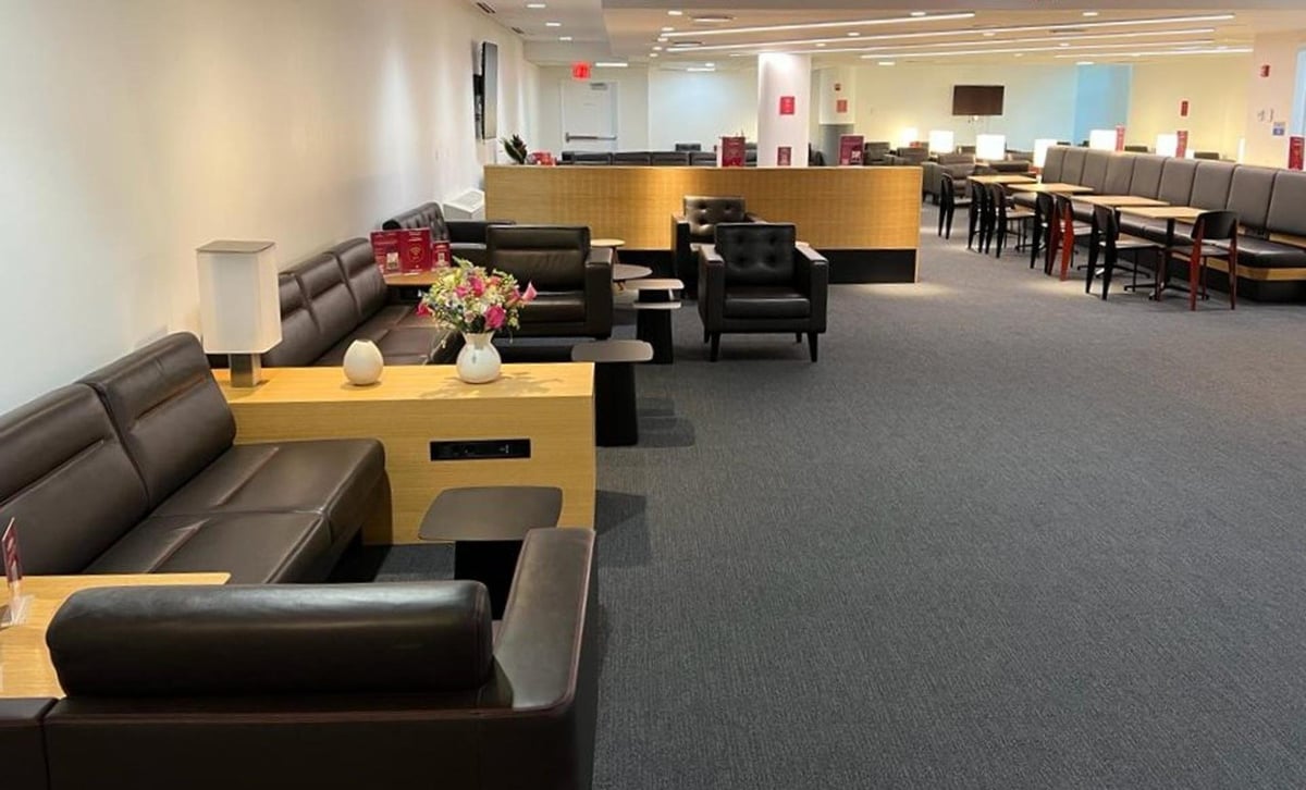 The seating area in the Primeclass Lounge at Terminal 4, JFK Airport, displaying a variety of brown leather seats and booths with black and wood accent tables. A vase with fresh flowers adds a touch of color to the muted tones of the room.