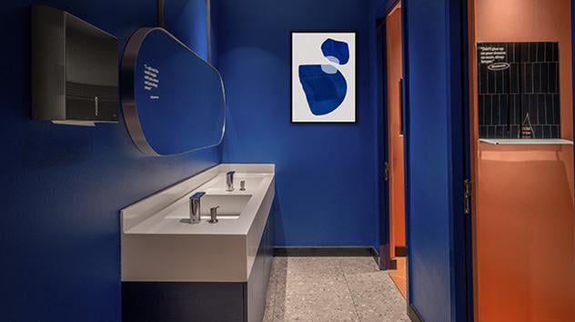 Restroom area at the Satellite Kepler Club, KUL airport. There is a sleek blue and rust wall colour scheme, dual sink vanity, minimalist artwork and an individual private shower or bathroom stall.