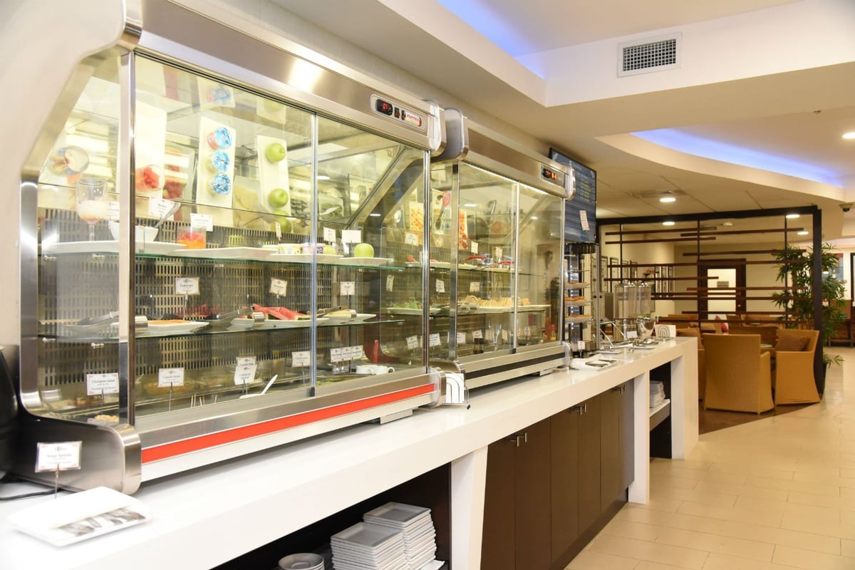 Buffet area at Club Kingston Lounge, Norman Manley International Airport, featuring chilled display cases with snacks, fruits, and beverages in a modern, comfortable setting.