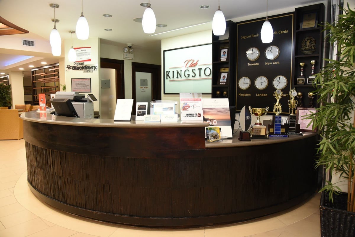 Reception desk at Club Kingston Lounge in Norman Manley International Airport, featuring international clocks, awards, and travel brochures in a modern, welcoming setting.