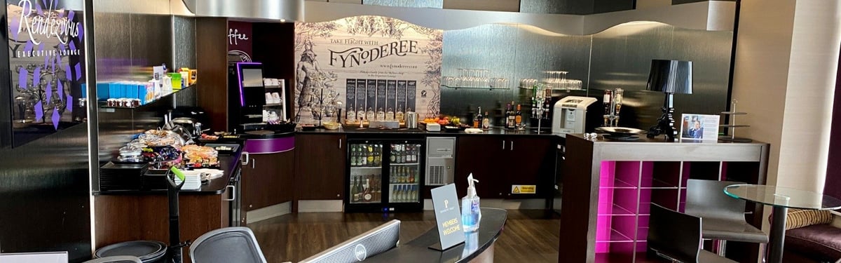 The buffet section at the Rendezvous Lounge at IOM airport. Pink LED lights add a stylish glow to the counters. There is a self serve coffee machine and mini bar, as well as a selection of food stuffs.