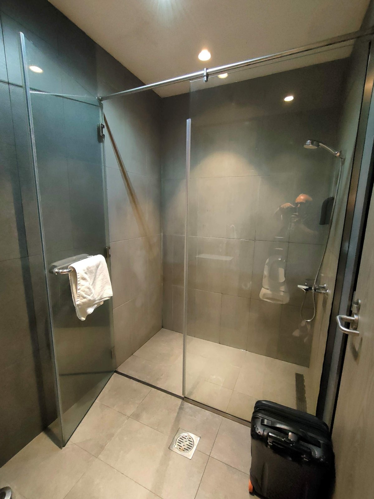 The image shows a modern and clean shower stall at the Plaza Premium Lounge at DXB airport. The shower area is enclosed by sleek glass doors and features neutral toned tile walls and flooring giving it a minimalist and polished look.