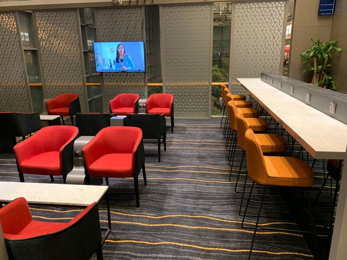 Seating area inside Marhaba Lounge at Singapore Changi Airport Terminal 3, featuring red armchairs, work counters with charging outlets, and a TV screen.