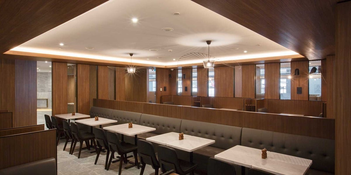 Dining area of the Plaza Premium Lounge at Melbourne Airport. Dark wooden floor and ceilings add a natural, comfortable feel. There are marble tables and a variety of chairs for seating.