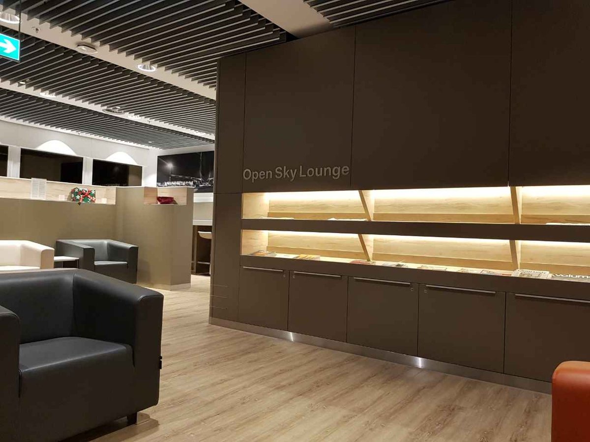 Modern Open Sky Lounge at Düsseldorf Airport with leather armchairs, wooden flooring, and a softly lit magazine wall.