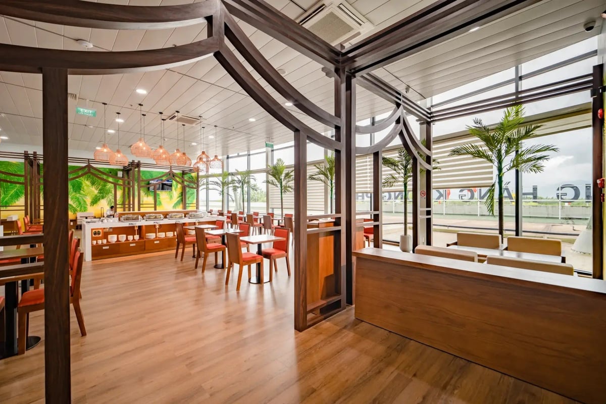 Spacious dining area in the SH Premium Lounge at Phu Cat Airport (UIH), with wooden tables, orange chairs, a buffet station in the background, and large windows overlooking the tarmac.