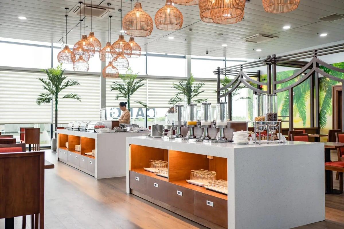Buffet area in the SH Premium Lounge at Phu Cat Airport (UIH), with two white counters displaying food warmers, beverage dispensers, glassware, and decorative wicker pendant lights.