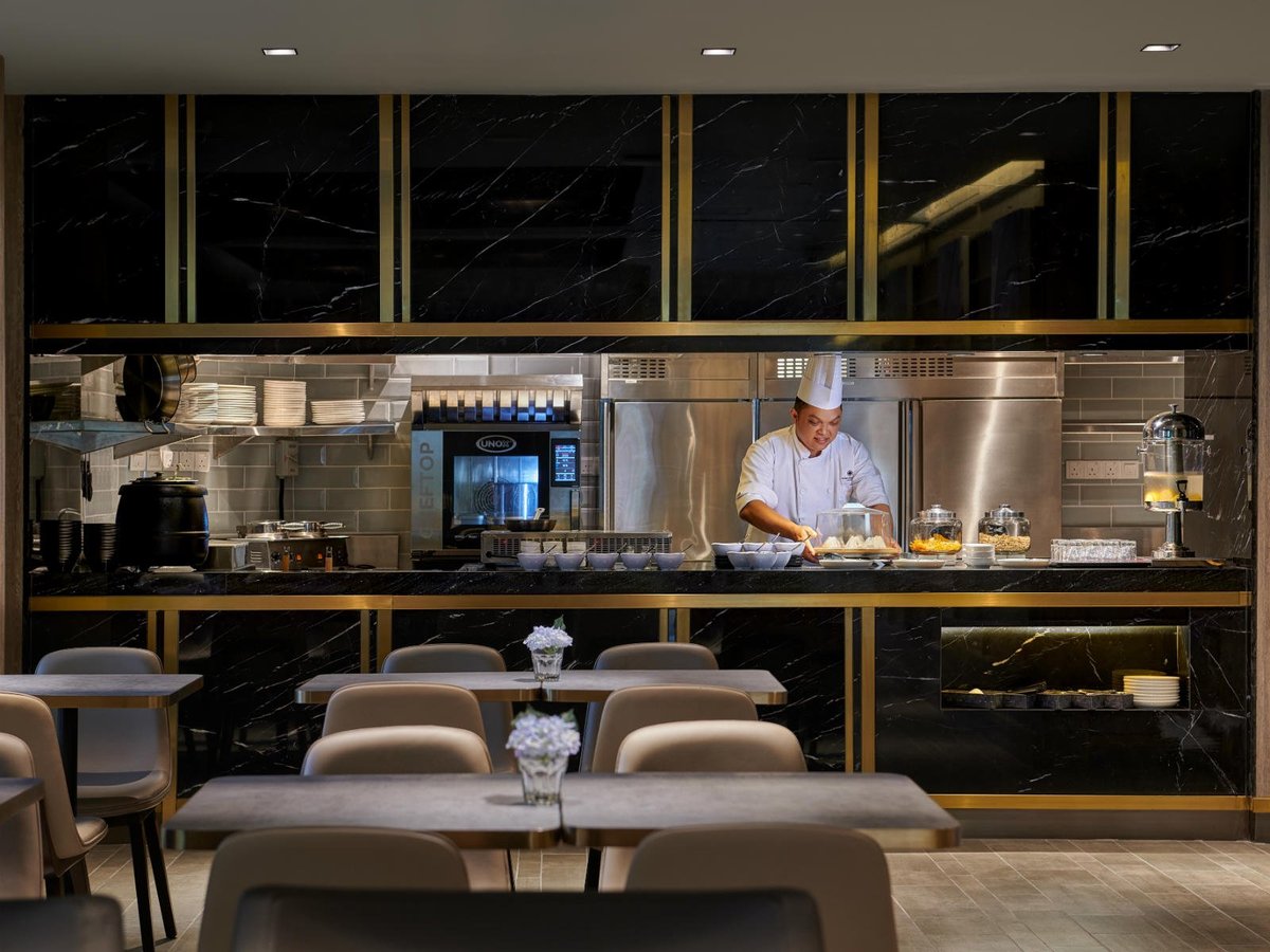 The buffet area at the Plaza Premium Lounge at Adelaide Airport. Fresh salads, vegetables, pasta and bread can be seen in open containers on marbled countertops. People can be seen in the background socialising and drinking on high bar stools.