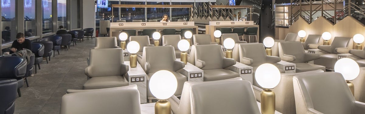 Plaza Premium Lounge at Sabiha Gökçen International Airport, highlighting its sophisticated design and relaxing ambiance. The lounge features a mix of deep blue and neutral beige armchairs, each paired with round, golden floor lamps.