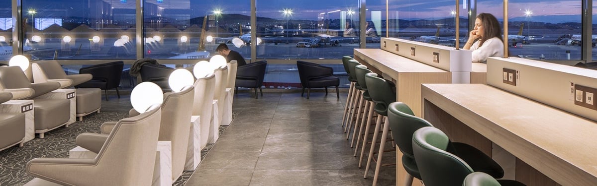 This image captures the tranquil and modern atmosphere of the Plaza Premium Lounge at Sabiha Gökçen International Airport during twilight. The lounge area is bathed in soft natural light from the large windows that offer a panoramic views of runway.