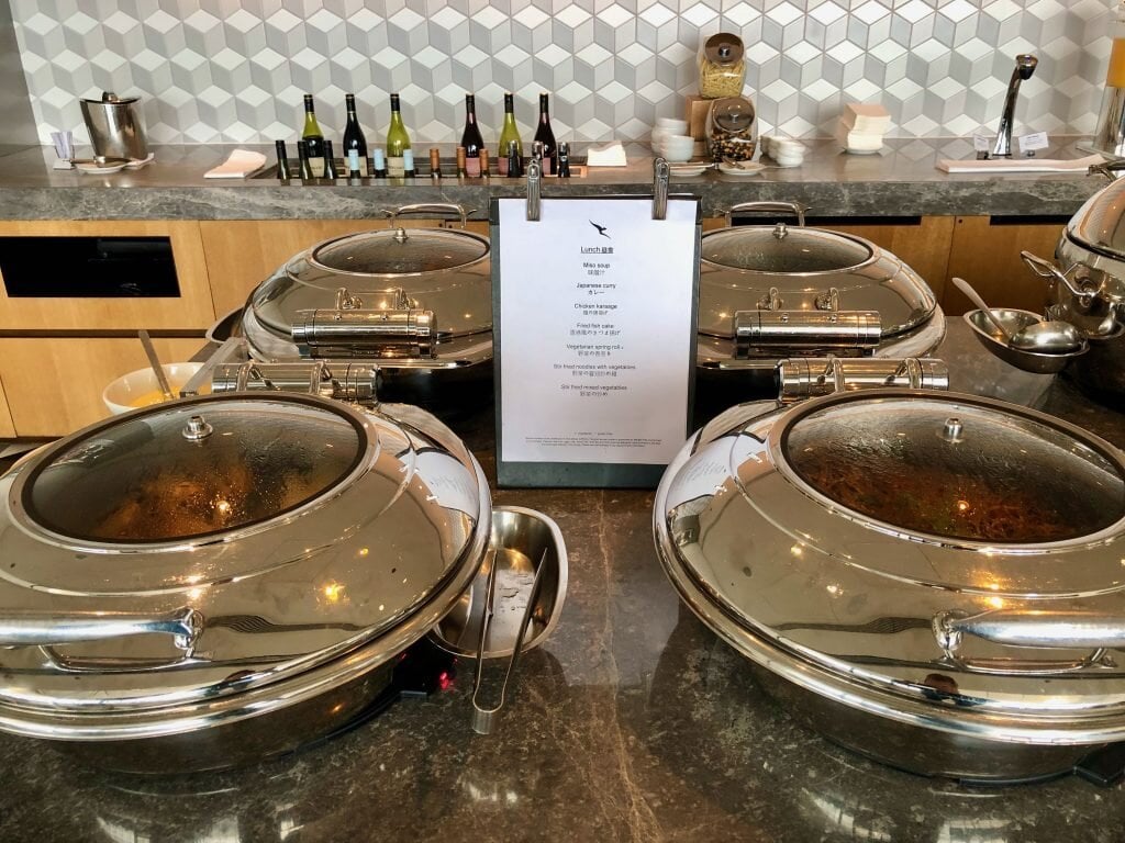 Hot buffet selection at the Qantas Hong Kong Lounge featuring stainless steel chafing dishes and a daily lunch menu with curries, mains, and vegetarian options.