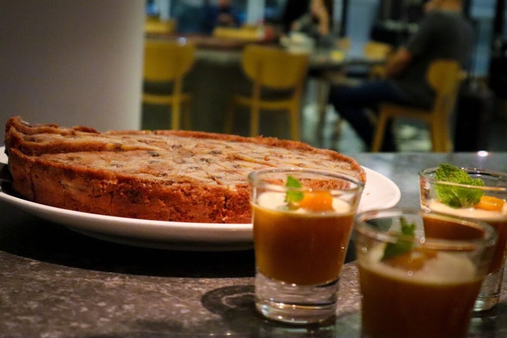 Fresh desserts at the Qantas Hong Kong Lounge, featuring a large plate of banana bread pudding and individual glasses of mango panna cotta garnished with mint leaves, set on a stone countertop.