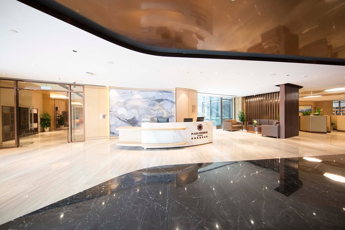 Entrance to the Plaza Premium VIP Lounge at Qingdao Jiaodong International Airport, featuring a modern reception desk, marble floors, and a sophisticated interior design with comfortable seating areas.