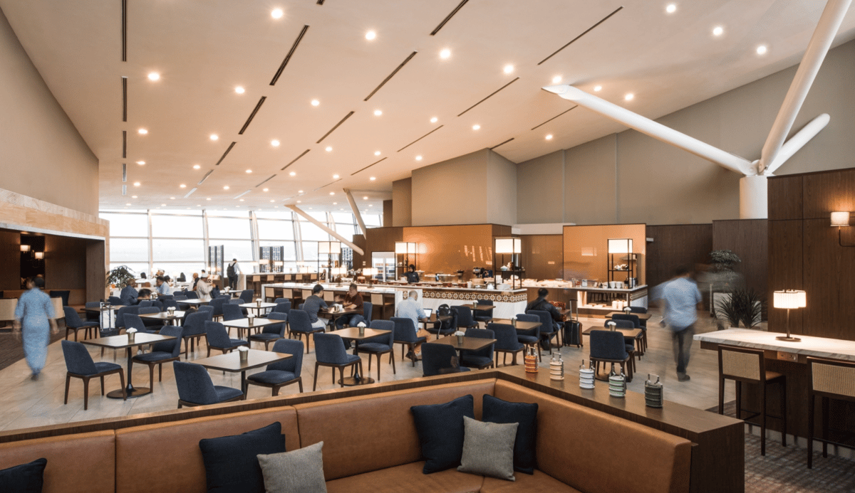 Modern dining area of the regional or contact pier Malaysian Airlines Golden Lounge at KUL airport featuring a buffet in the background and a beige leather sofa in the foreground. Between the two is a dining area with blue seats.