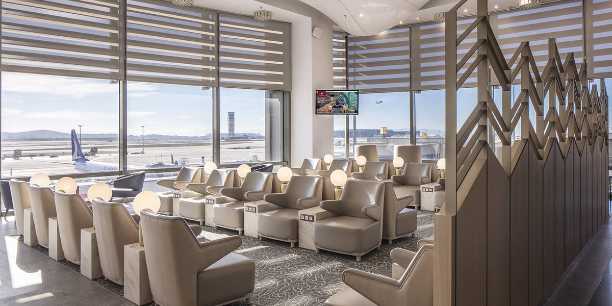 Airport lounge with views of tarmac, plush seating, decorative wooden walls.