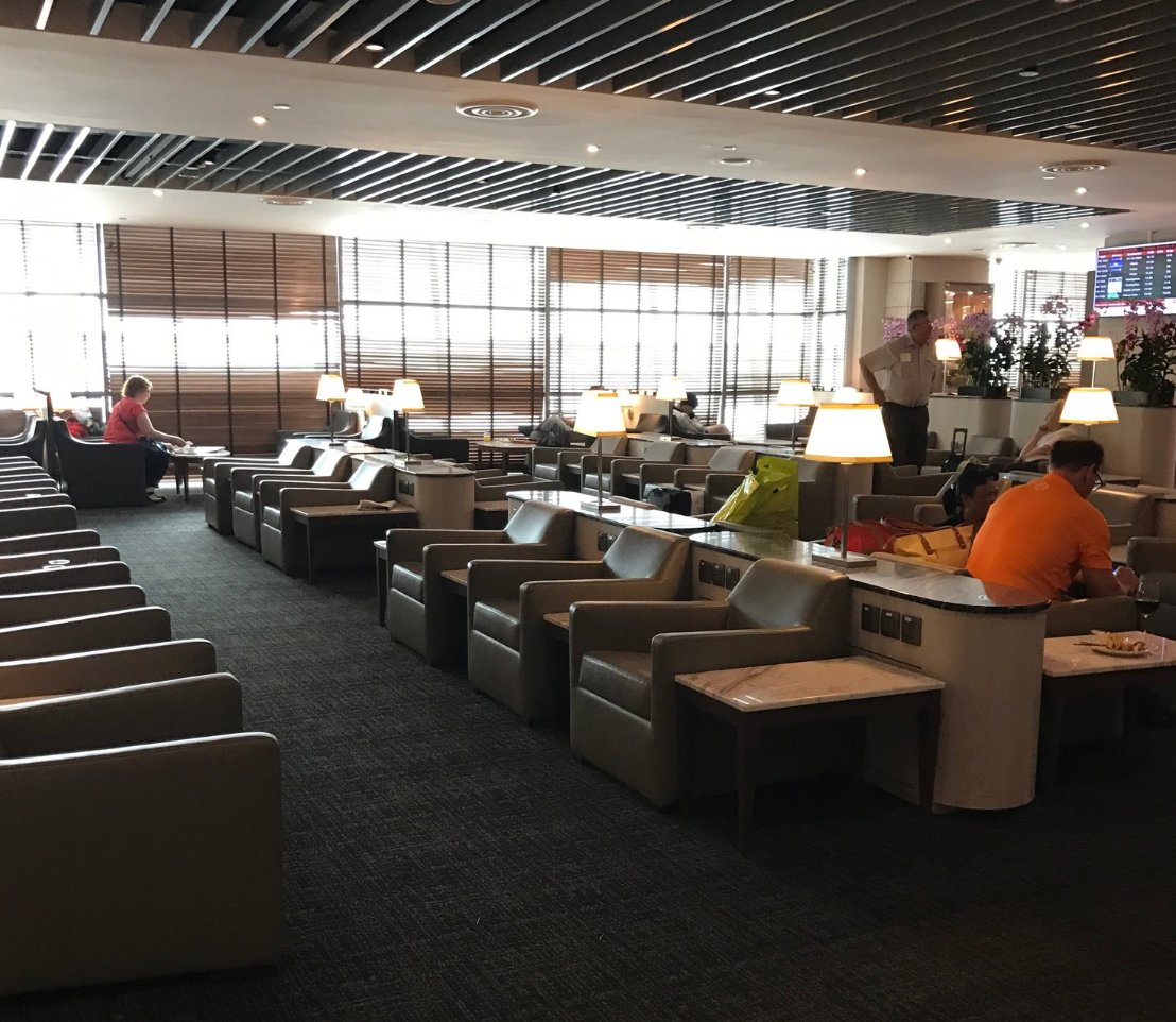 Spacious seating area at SATS Premier Lounge Terminal 2 Changi Airport, featuring rows of plush armchairs with marble side tables, warm table lamps, and natural light.