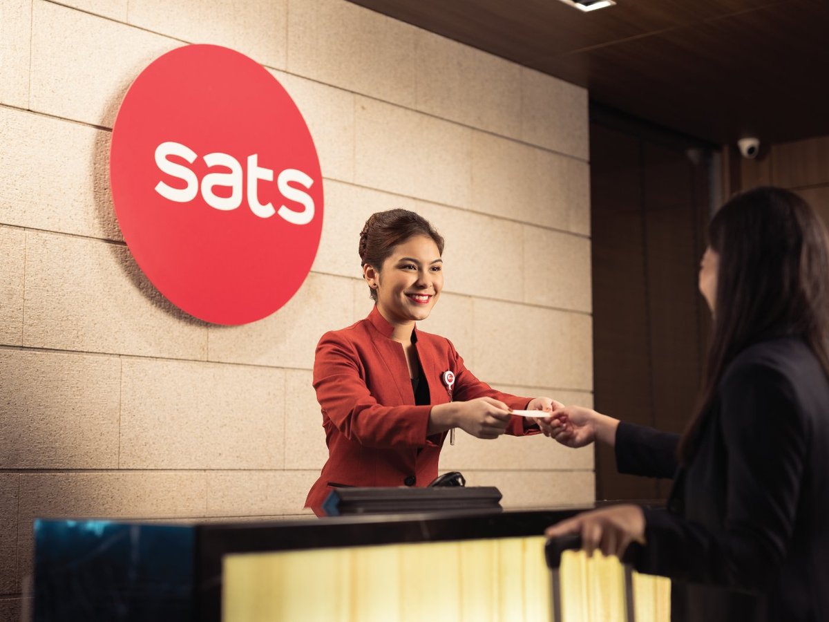 SATS Premier Lounge reception at Changi Airport Terminal 2 with a friendly staff member in red uniform assisting a passenger at check-in desk