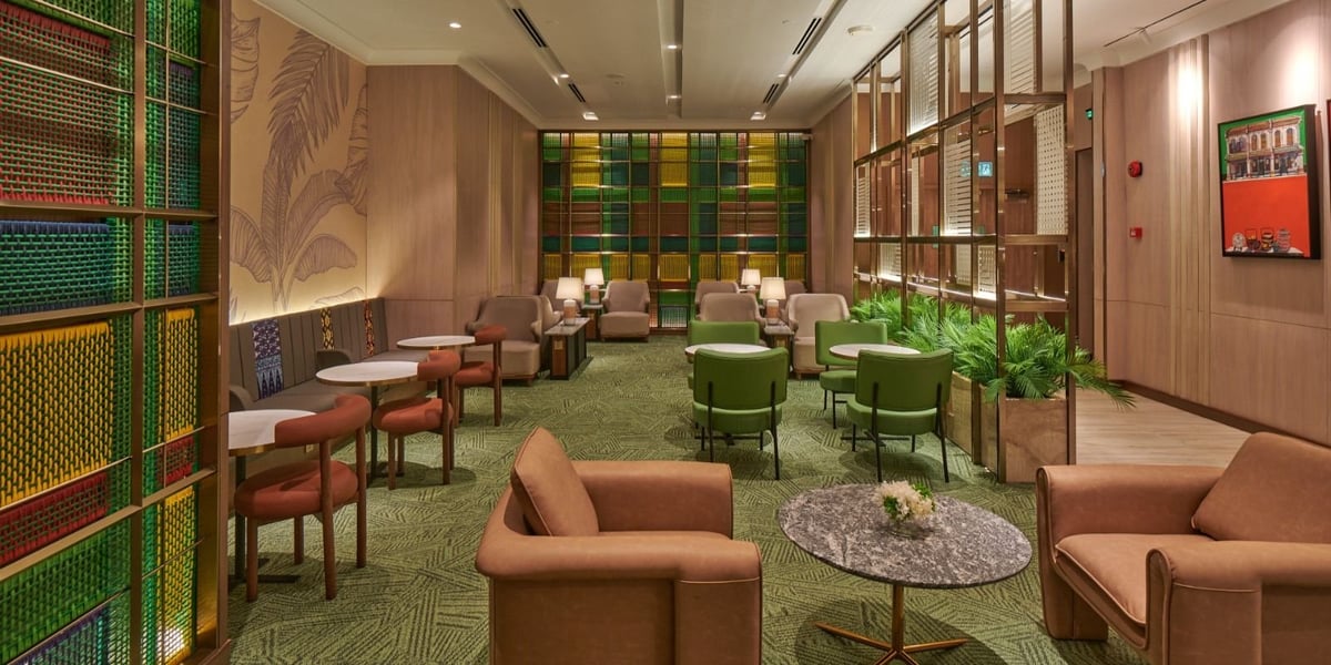 Stylish seating area at the Plaza Premium Lounge T1 at Kuala Lumpur Airport, featuring a mix of modern armchairs in neutral tones, batik-patterned accents, and colourful woven wall panels in the Malaysian design.