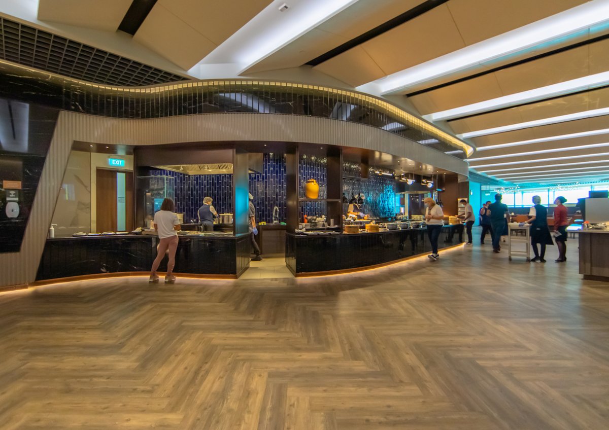 Buffet and dining area inside the SilverKris Business Class Lounge at Singapore Changi Airport, featuring modern lighting, wooden flooring, and a variety of food stations.