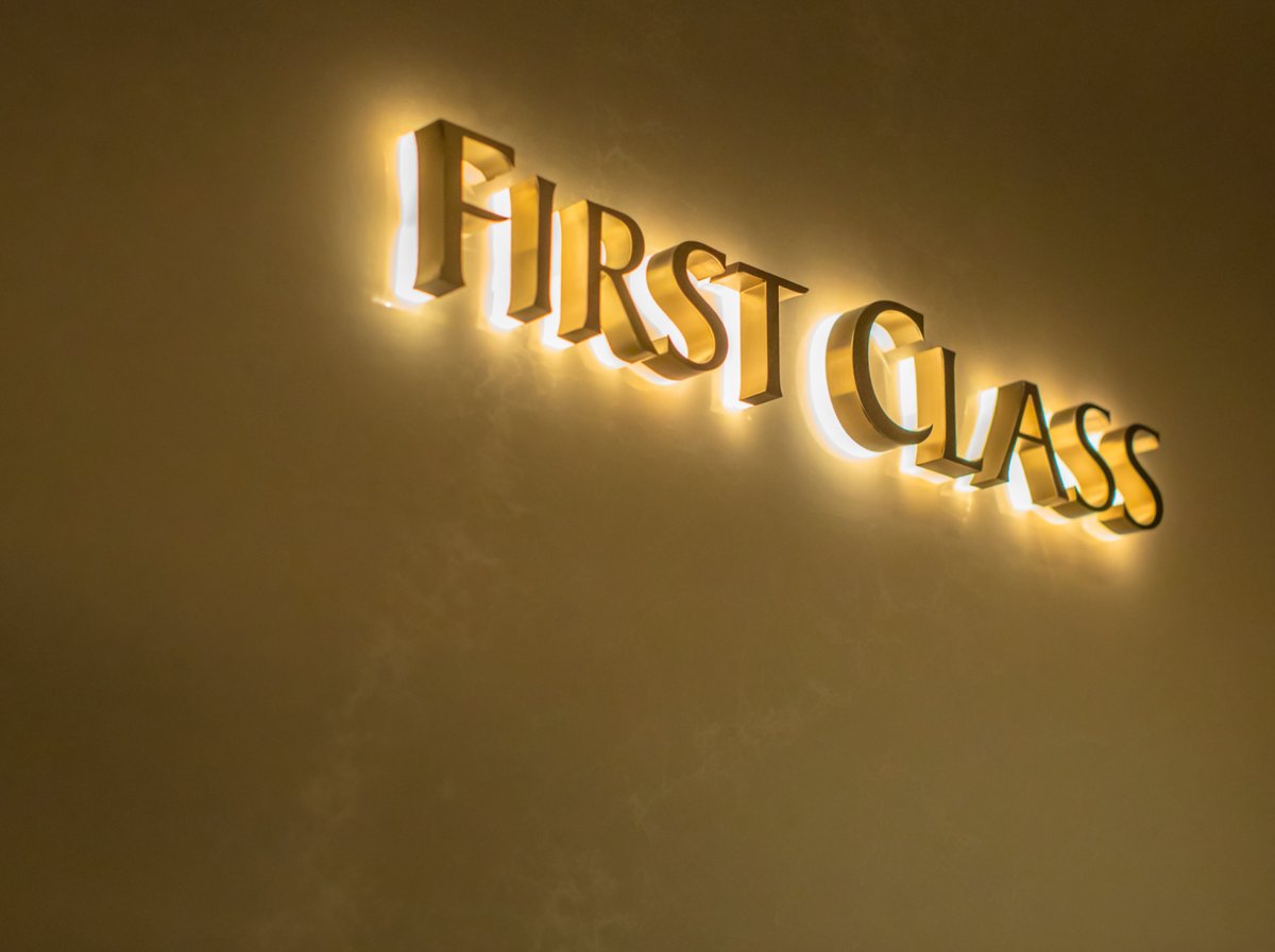 Elegant gold backlit sign reading ‘First Class’ on a marble wall at Singapore Changi Airport, symbolizing premium luxury travel.