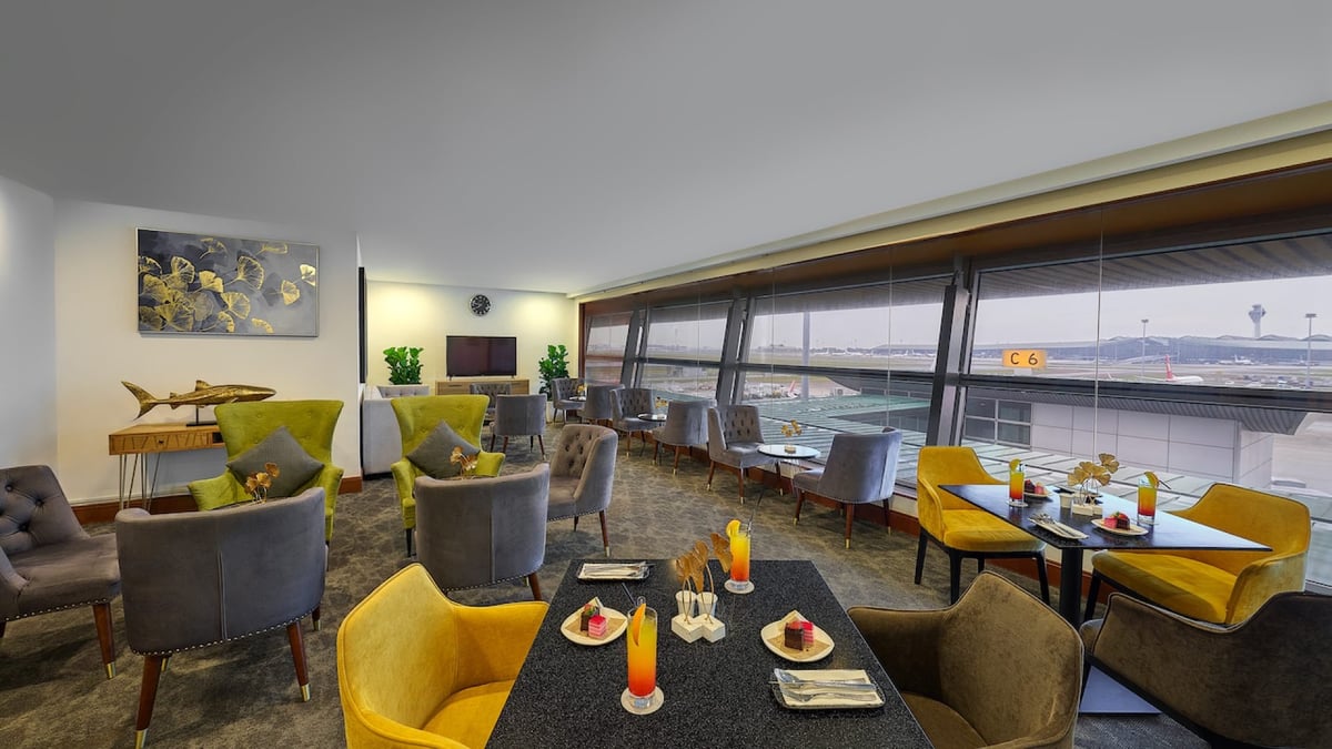 Bright dining and lounge area at the sky suite satellite terminal Kuala Lumpur Airport, featuring colourful upholstered chairs, large windows with airport runway views, and has a relaxed, modern ambiance.