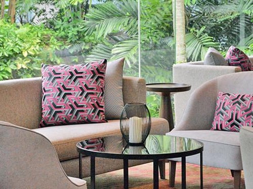 Sphere Lounge grey sofas with pink and black geometrically designed pillows and a glass table with a candle between the seats.