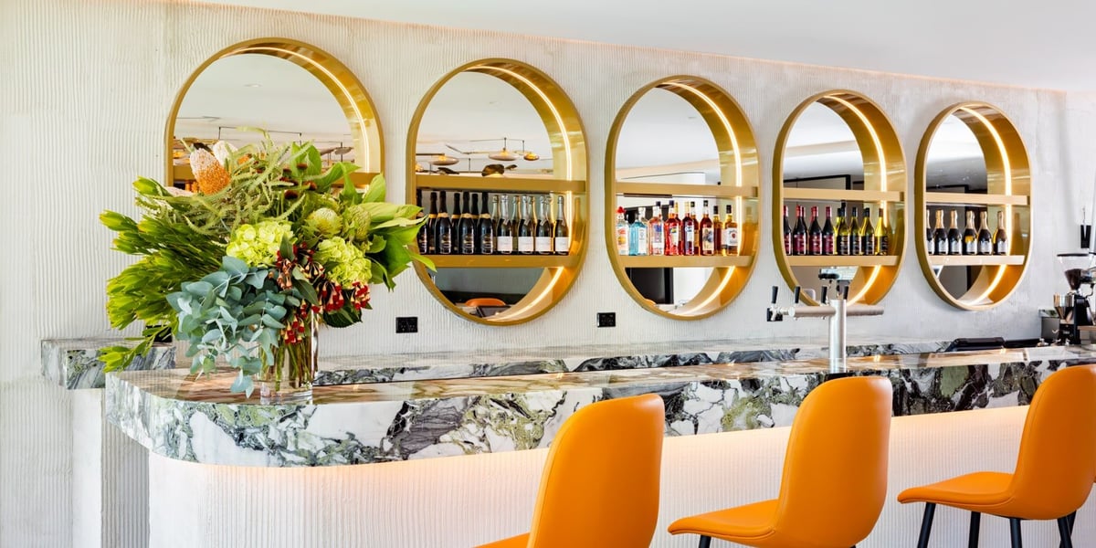 Plaza Premium Lounge at Sydney Airport highlighting the bar and dining section of the lounge. Grey and green tiled styles make up the decor with an arrangement of alcoholic beverages seen behind the bar.