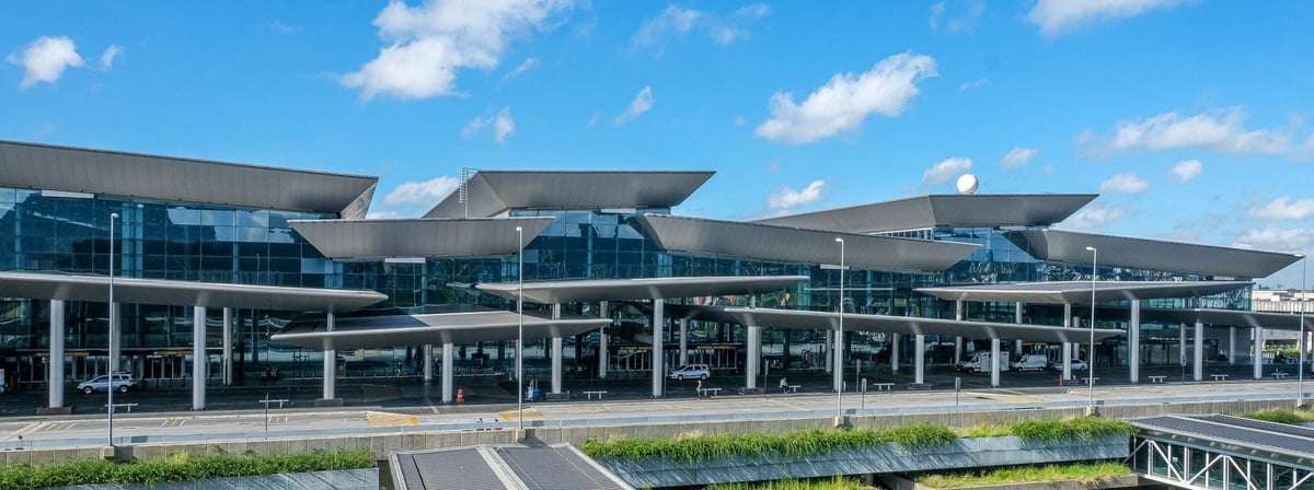 Exterior view of Terminal 3 at São Paulo Guarulhos International Airport (GRU), featuring modern glass façade and unique angular roof design under a bright blue sky.