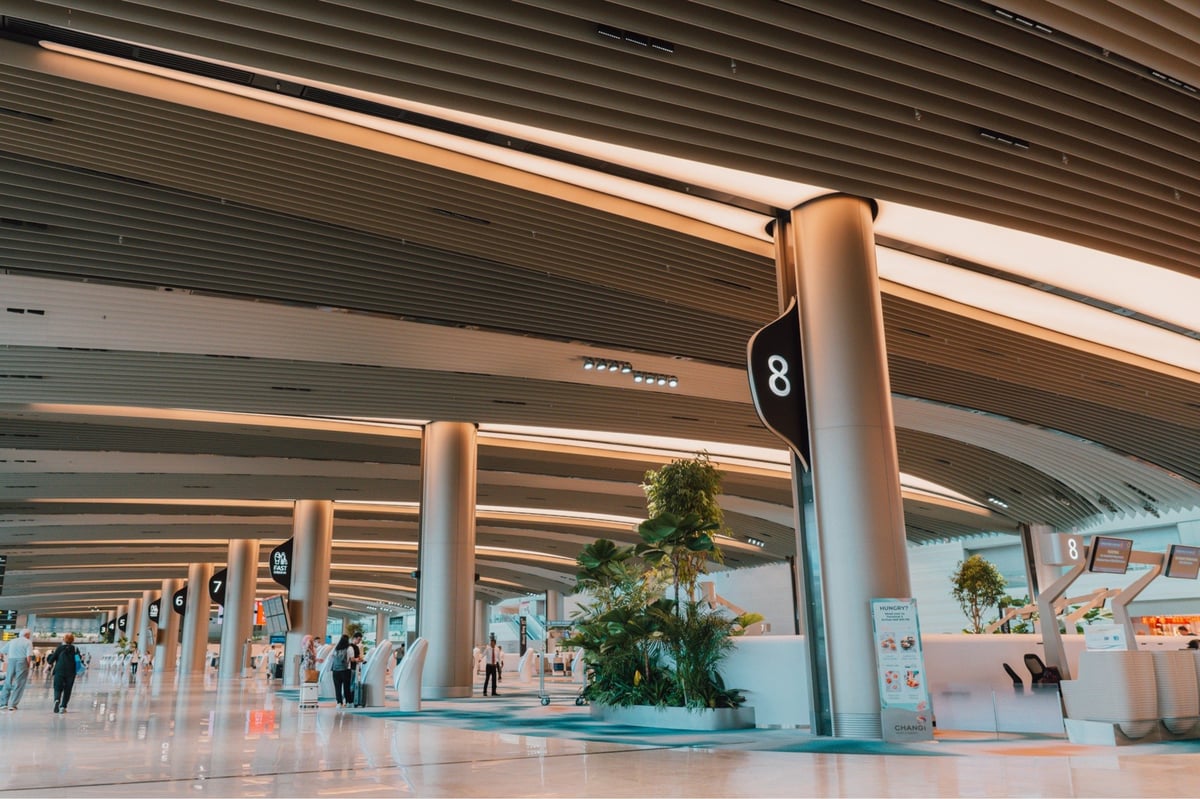 Modern check-in area at Changi Airport with sleek design, greenery, and automated kiosks under curved ceiling architecture.