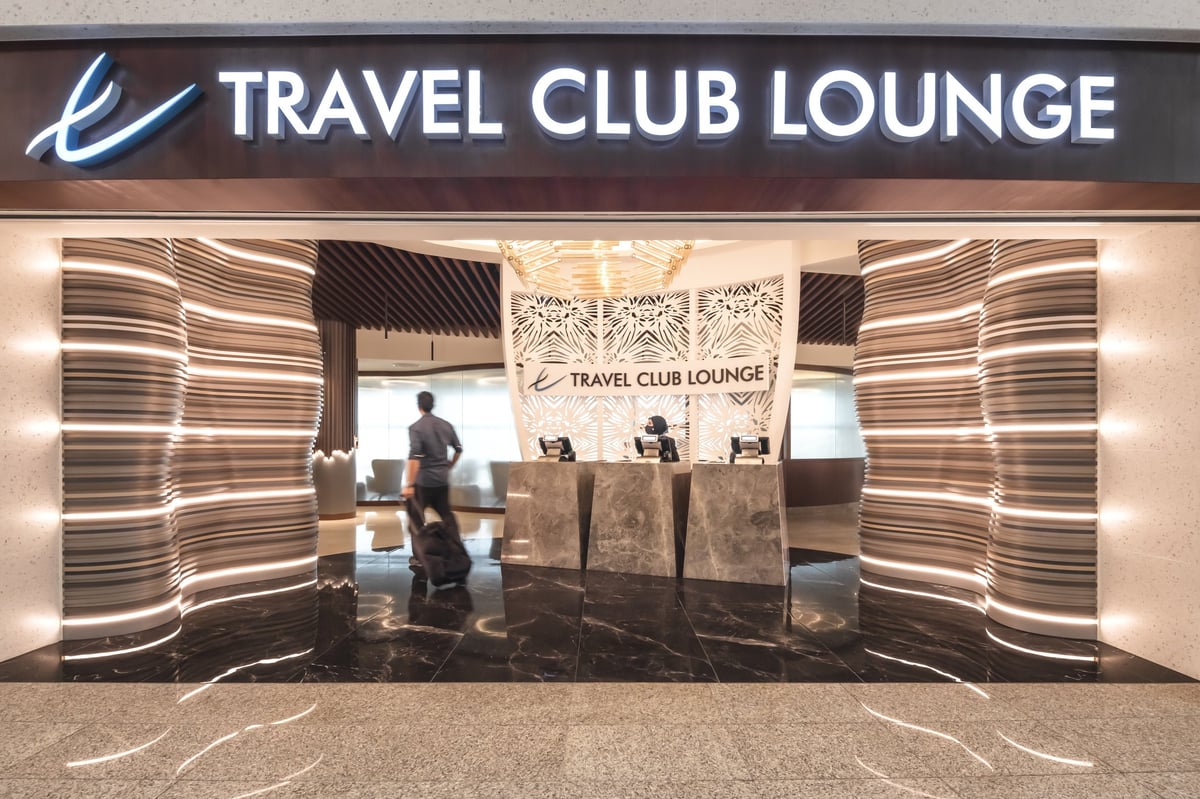 Entrance to the Travel Club Lounge at KLIA’s Satellite Terminal, showcasing a sleek, modern design with wave-textured illuminated walls, marble floors, and a decorative white reception backdrop with floral patterns.