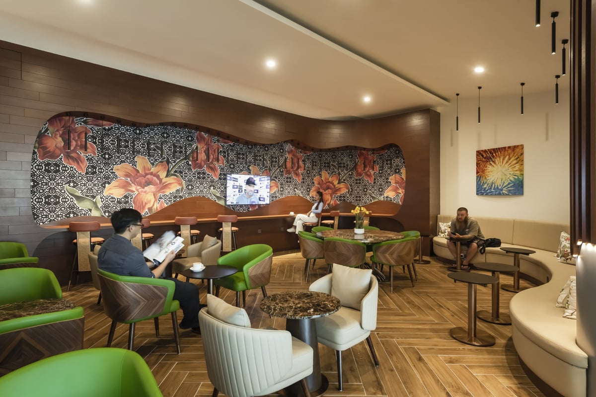 Colourful seating area inside the Travel Club Lounge at KLIA’s Satellite Terminal, featuring bold floral wall art, wood paneling, green and cream armchairs, and a cozy café-style layout with marble-top tables and soft lighting.