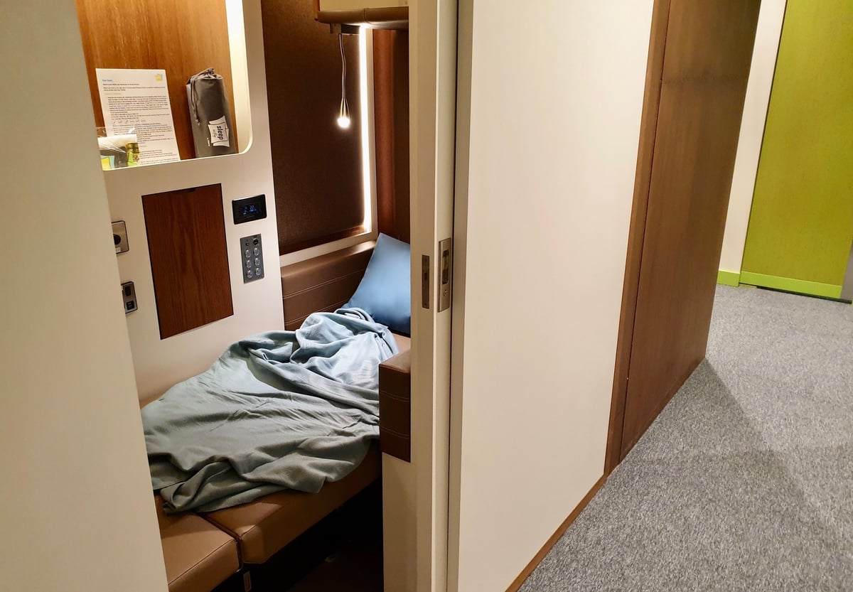 Flexisuite pod at sleep 'n fly DXB Airport with bed lying down, pillow and blanket, and light on