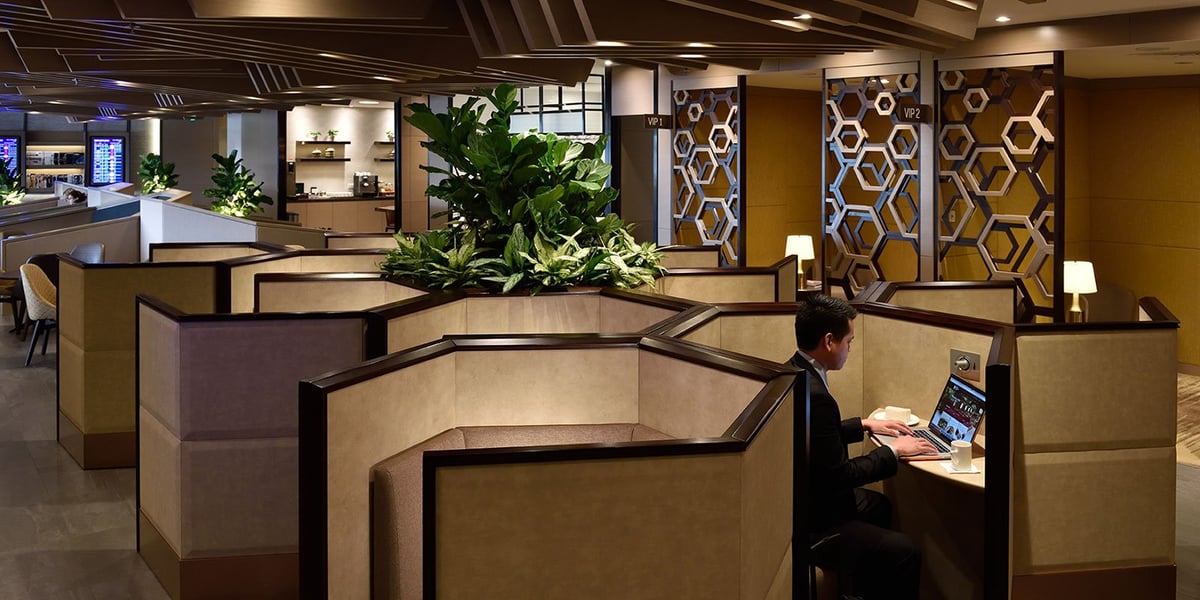 Seating pods in the Plaza Premium Lounge at Changi Airport. Warm lights emanate from the pods and lush greenery can be seen evenly spaced between subsections of the lounge. Abstractly shaped partitions can be seen in the right background.
