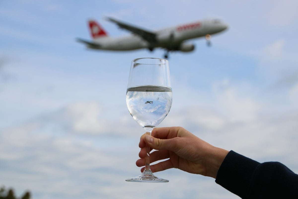 Glass being held up against a sky with an aeroplane flying in the background
