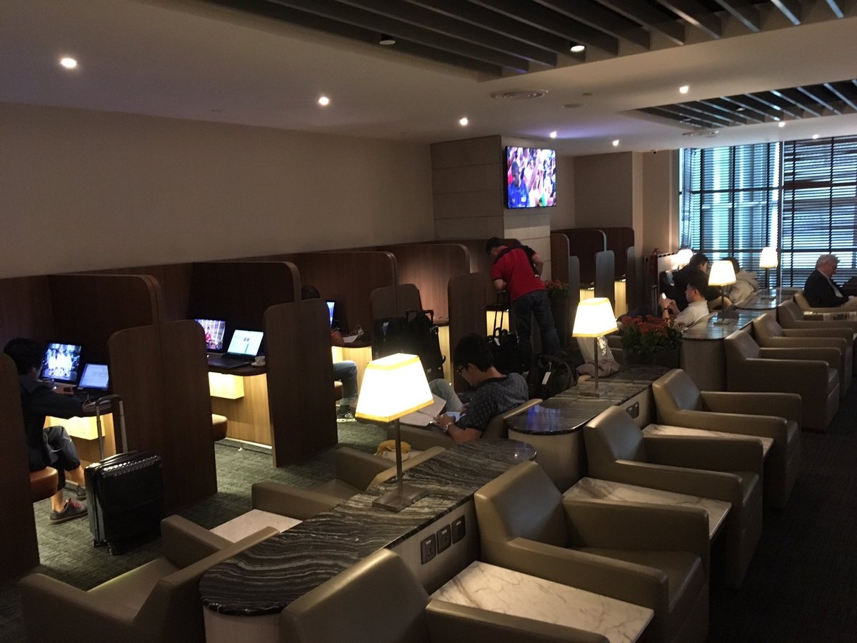SATS Premier Lounge Changi Airport Terminal 2 workstations with individual cubicles, laptops, and adjacent lounge armchairs with marble-topped side tables.