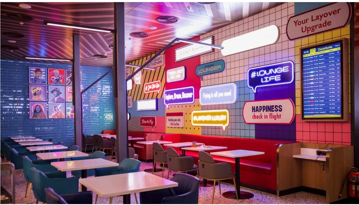 Gate Z Lounge at Bengaluru International Airport (BLR) featuring a vibrant dining area with modern seating, neon wall signage, and digital flight information displays.