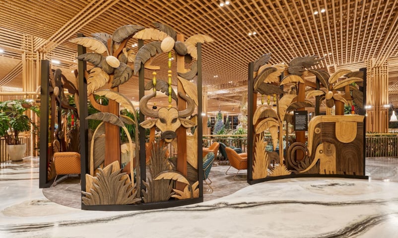 The Kabini Relaxation Lounge at 080 T2 BLR airport, depicting intricate carvings of wildlife, including a bull, an elephant, and tropical foliage. The partitions are part of the airport's lounge decor, creating a natural, earthy ambiance.