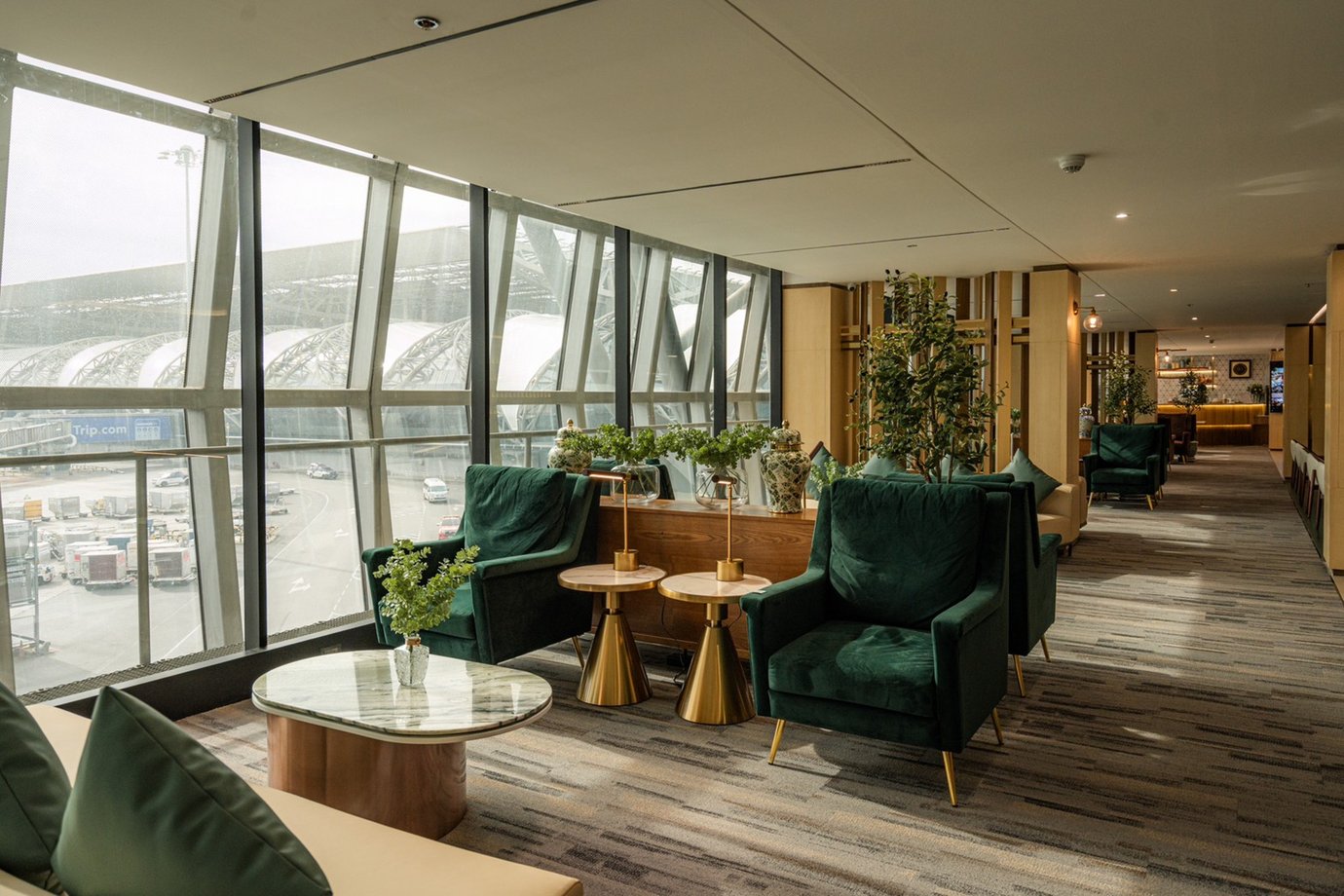 Window-side seating inside The Coral Finest Business Class Lounge at Bangkok Suvarnabhumi Airport, featuring plush green armchairs with gold side tables, indoor plants, and panoramic glass windows. Window-side seating inside The Coral Finest Business Class Lounge at Bangkok Suvarnabhumi Airport, featuring plush green armchairs with gold side tables, indoor plants, and panoramic glass windows.