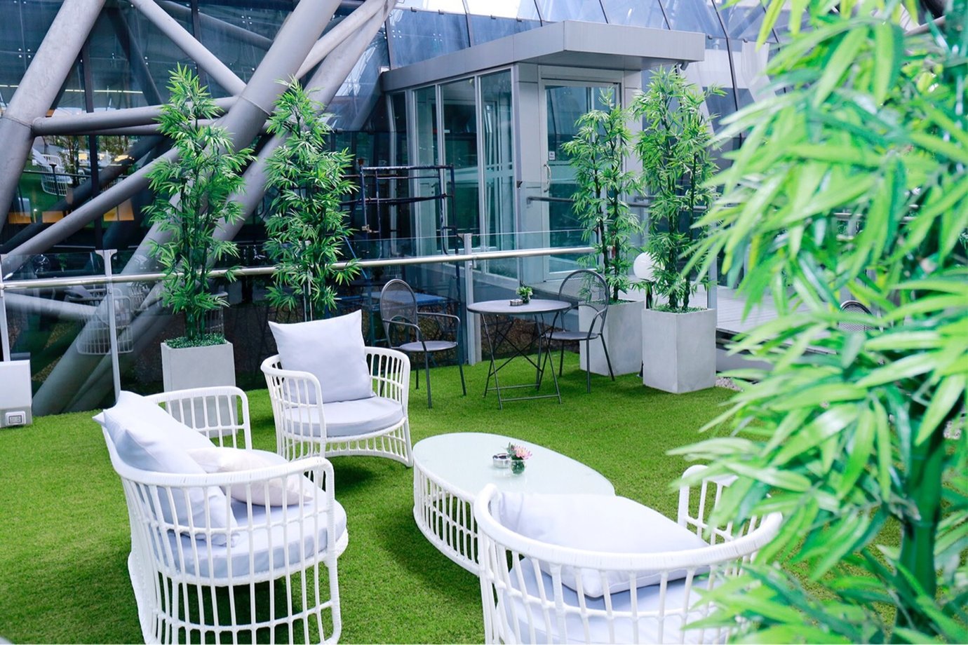 Outdoor terrace at the Miracle Business Class Lounge Concourse D Bangkok Suvarnabhumi Airport featuring white lounge chairs, green artificial grass, bamboo plants, and a relaxing open-air seating area with natural light. Outdoor terrace at the Miracle Business Class Lounge Concourse D Bangkok Suvarnabhumi Airport featuring white lounge chairs, green artificial grass, bamboo plants, and a relaxing open-air seating area with natural light.